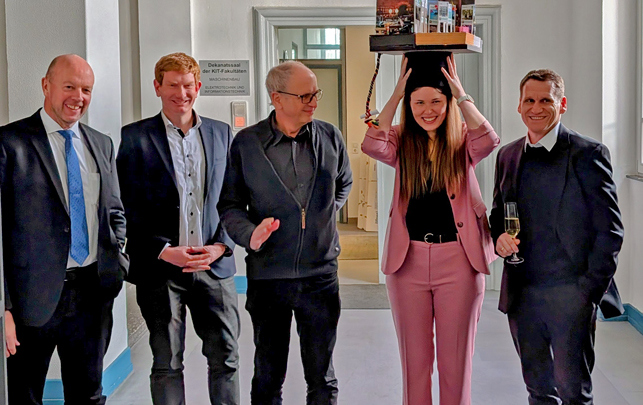 Gruppe von fünf Personen im Flur; eine Frau trägt einen Gegenstand auf dem Kopf, alle schauen Richtung Kamera.