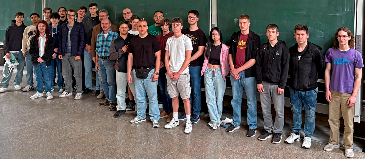 David Heger Eine Gruppe Personen steht vor einer Tafel in einem Klassenzimmer.