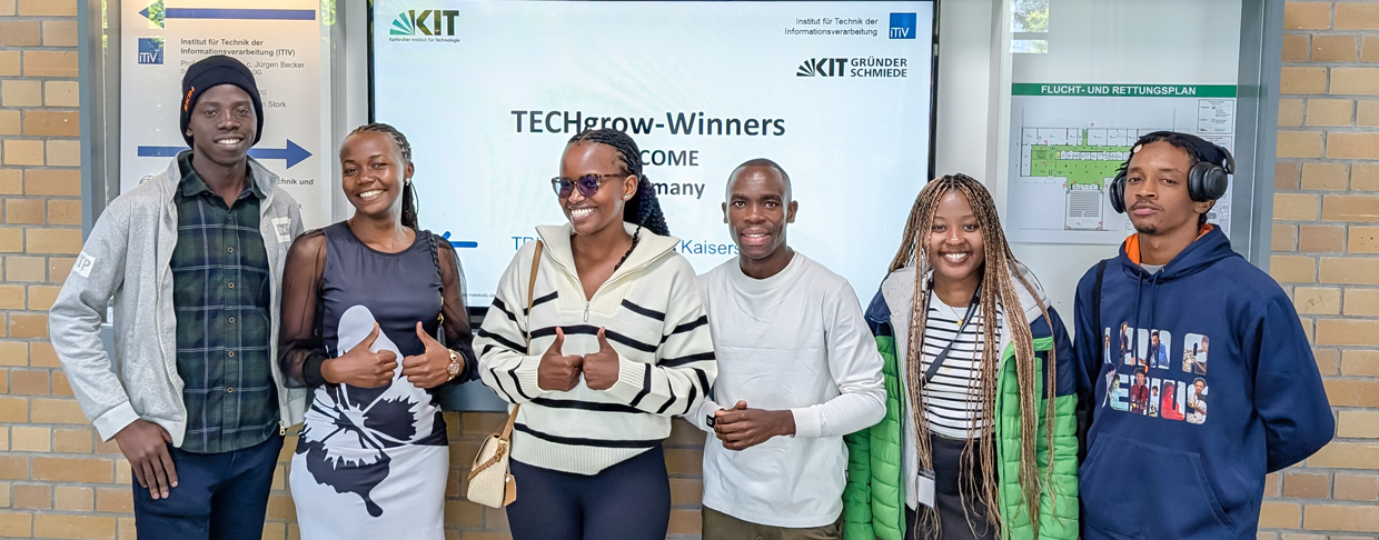 Gruppe junger Menschen vor Bildschirm mit TECHgrow-Winners Begrüßung am KIT Gebäude.